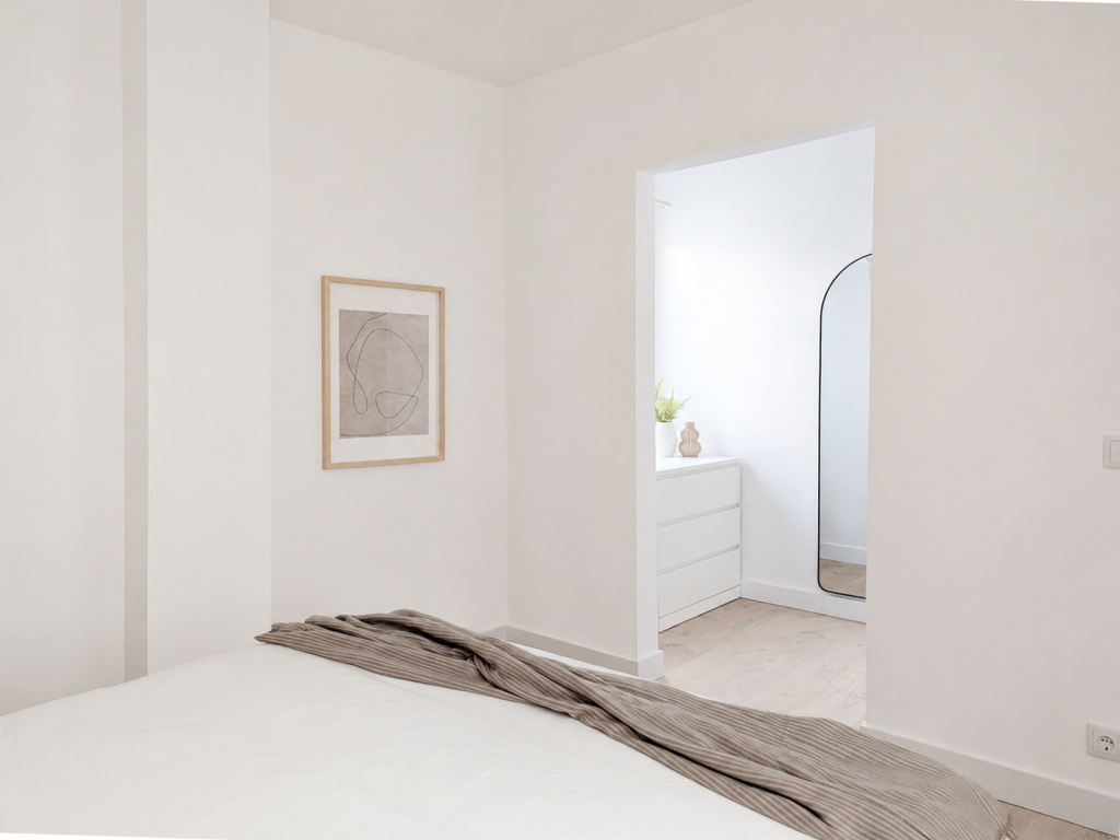 Vestidor abierto en blanco con cómoda integrada, espejo arqueado de perfil negro y acceso directo al dormitorio