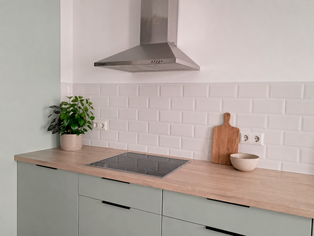 Cocina de apartamento con muebles verde suave, encimera de madera y frente de azulejos blancos.